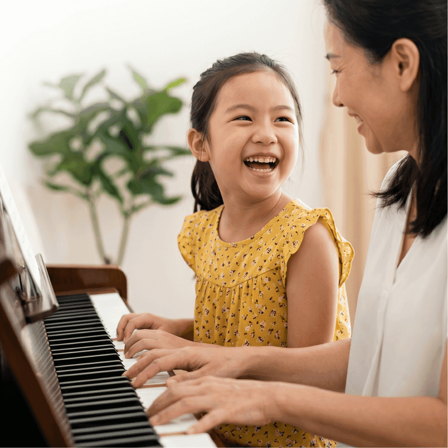 Happy child playing piano with her mom