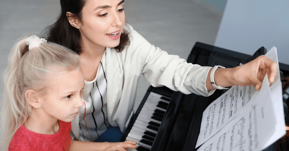 A piano teacher sitting with a young student at a piano